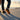 Pulse barefoot sneaker for men in black with gum sole, worn on a seaside promenade at sunset, rear three quarter view