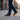 Pulse barefoot sneaker for men in black with gum sole, worn crossing a city street with a coffee cup, three quarter view