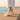Grove barefoot sneaker in peach pink with white sole, side view on a seaside wall
