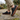 Sage barefoot sneaker in black tartan worn on a garden path, side view