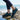 Cascade barefoot sneaker in black with teal blue, worn on a rocky seaside shore