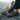 Trailblazer barefoot hiking shoe for men in dark grey with orange, worn seated at a mountain summit, side view