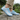 Summit barefoot hiking shoe in light blue, side view worn on a stone path