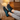 Cascade barefoot sneaker in black with teal blue, worn with feet up in a cozy room