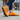 Stride barefoot sneaker in orange knit with brown sole, worn walking a city sidewalk