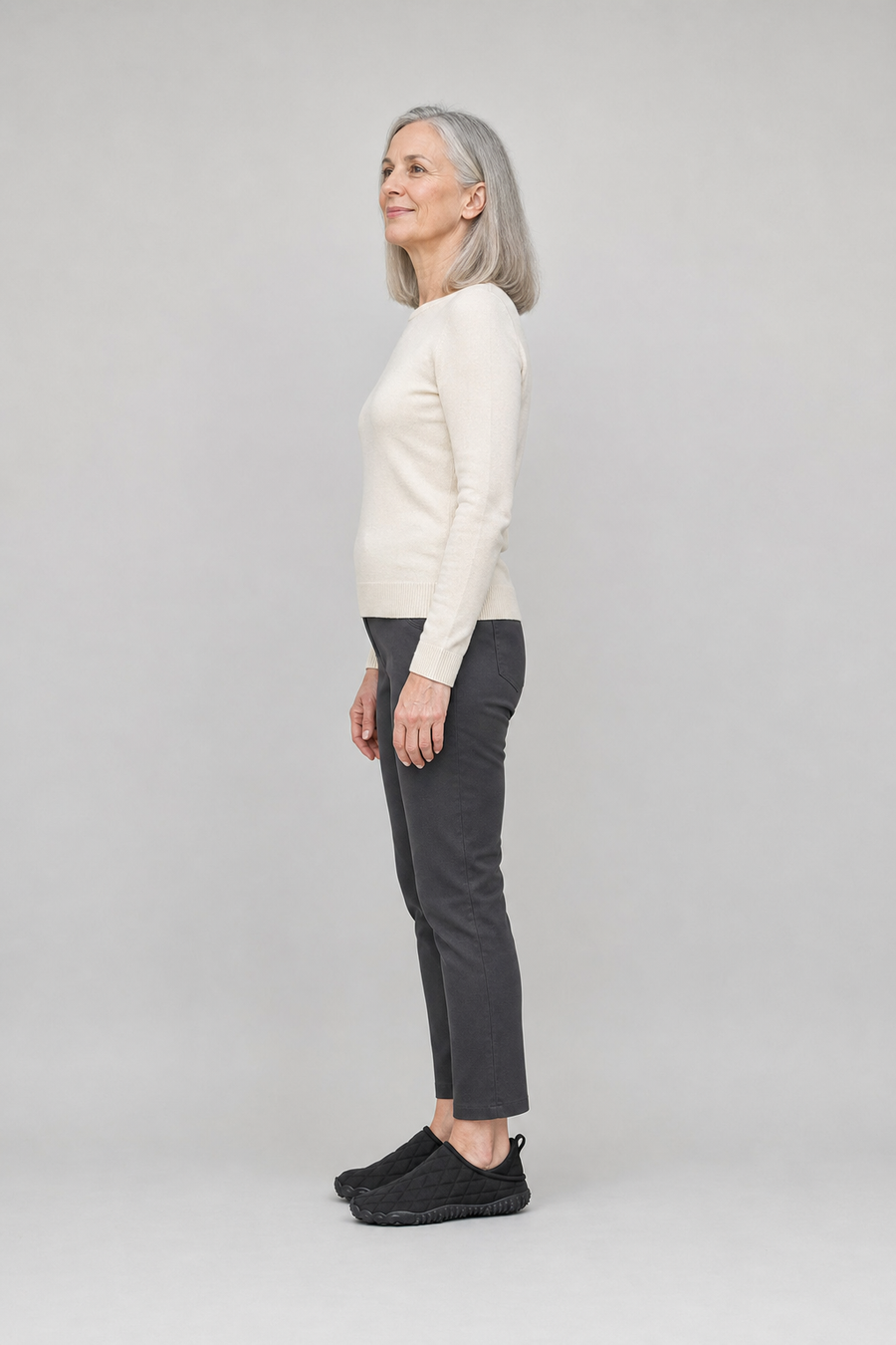 A woman standing in the Flow shoes, side view showing her hips, knees, ankles and the ball of her foot